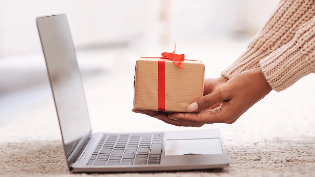 Black Friday 2026 en WooCommerce y Shopify: la checklist técnica 2 Manos entregando un paquete regalo junto a un portátil: preparar la tienda online para el Black Friday