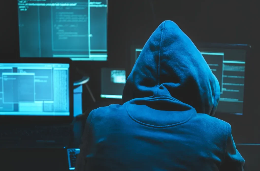 Black Hat SEO: qué es, qué penaliza Google y cómo salir 4 Persona encapuchada frente a varias pantallas en penumbra, imagen de las prácticas de black hat SEO