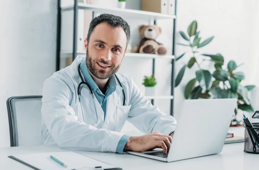 SEO para médicos y clínicas: cómo captar pacientes cumpliendo la ley 5 Médico sonriente trabajando con un portátil en su consulta: SEO para médicos y clínicas